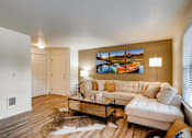 Thumbnail 2 of 34 - Apartments in Happy Valley, OR, for Rent - Sunnyside Village - Spacious Living Room with Wood-Style Flooring, Animal Skin Rug, Cream-Colored Sectional Couch, Wooden Coffee Table, Floor Lamp, Side Table with Lamp, White Walls with a Beige Accent Wall, and Large Window.