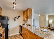 Thumbnail 9 of 34 - Happy Valley, OR, Apartments - Sunnyside Village - Kitchen with Wood-Style Flooring, Granite Countertops, Wood-Style Cabinetry, and Black Appliances.