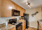 Thumbnail 7 of 34 - Apartments Happy Valley, OR - Sunnyside Village - a Kitchen with Wood-Style Flooring, Granite Countertops, Black Appliances Including a Refrigerator, Oven, Dishwasher, and Built-In Microwave, Brown Wood-Style Cabinetry, and an Overhead Lighting Fixture