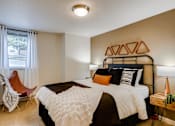 Thumbnail 11 of 34 - One Bedroom Apartments in Happy Valley, OR - Sunnyside Village - a Bedroom with Plush Carpeting, a Bed, Two Bedside Tables with Lamps, a Ceiling Lamp, and a Window with Binds and Curtains