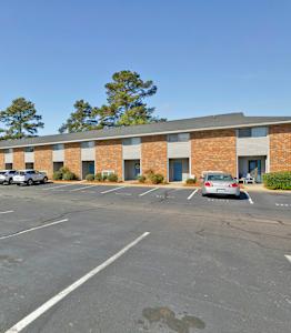 A parking lot with a building in the background and cars parked in the spaces.