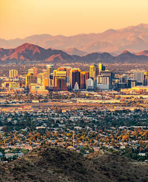 A cityscape with mountains in the background during sunset.