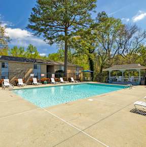 A swimming pool surrounded by trees and chairs.