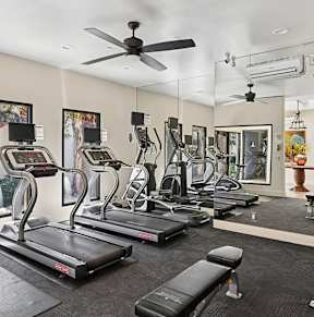 A spacious gym with treadmills, elliptical machines, and a ceiling fan.