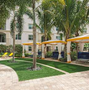 a courtyard with palm trees and yellow umbrellas in front of a building