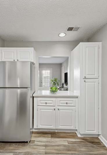 A kitchen with a refrigerator, cabinets, and a dining table.