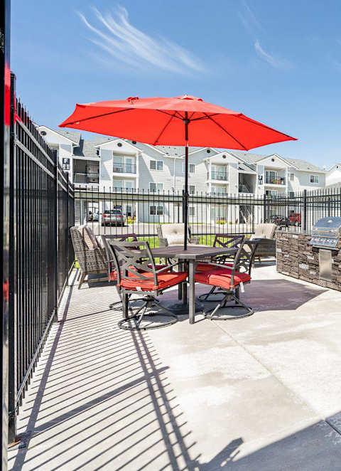 A patio with a red umbrella and chairs.