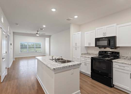 Peaks of Lexington Apartments Kitchen with Black Appliances, Granite Countertops and White Cabinetry and connected living room