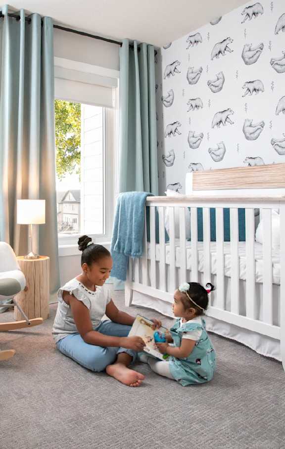 Two young girls sitting on the floor in a nursery room.
