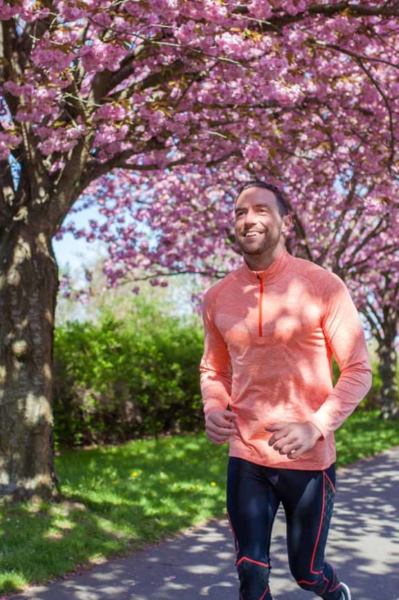 A man in a pink shirt and black pants runs down a tree-lined path.