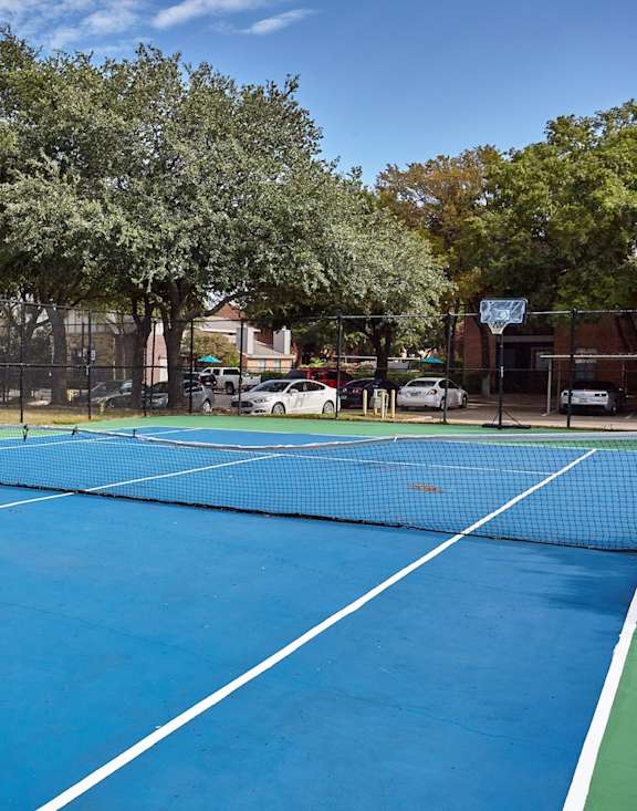 Blue sport court at Fusion Crossroads Apartments surrounded by a chainlink fence and trees