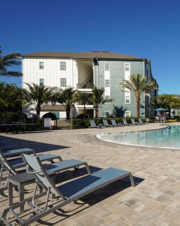 a resort style swimming pool with lounge chairs and umbrellas in front of a row of at Fountainhead, Jacksonville, FL, 32258