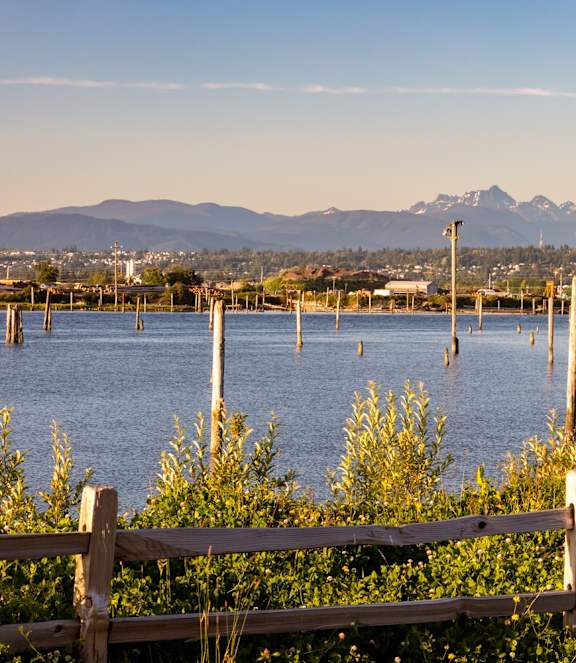 A wooden fence in front of a body of water with mountains in the background.