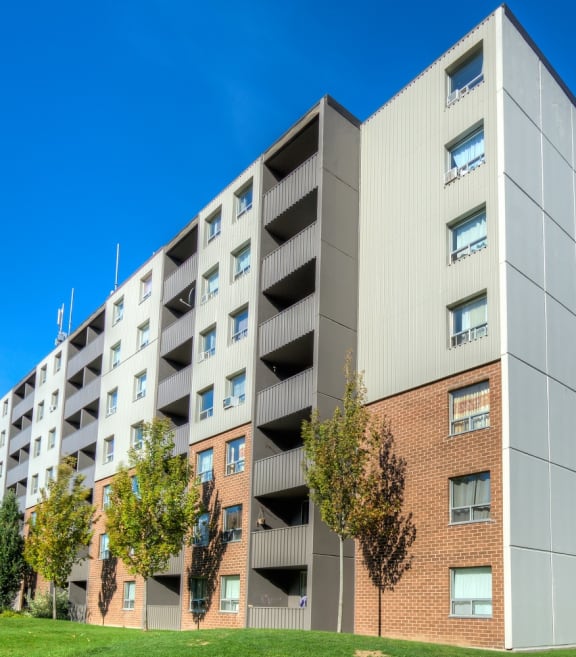 a large apartment building with trees in the foreground and a blue sky in the background at Platts Crossing, London, ON