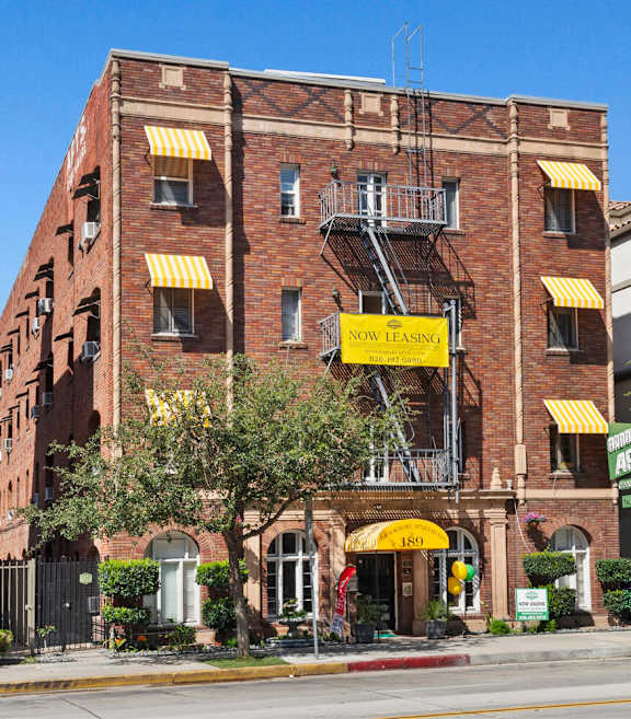 The exterior of Brookmore Apartments in Pasadena, CA with red brick and a yellow banner that says "Now Leasing" toward the top.