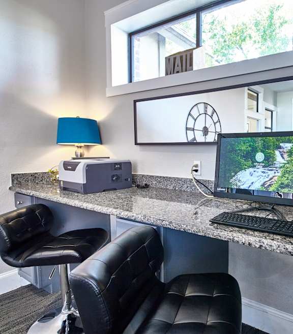 The business center at Fusion Crossroads with two black counter stools, a grey counterrop, and a computer and blue lamp