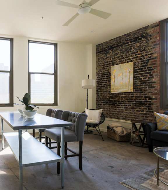 A kitchen with a refrigerator, a dining table with chairs, and a brick wall.