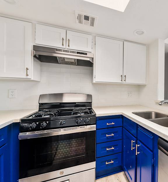 A kitchen with blue drawers and a stove top oven.