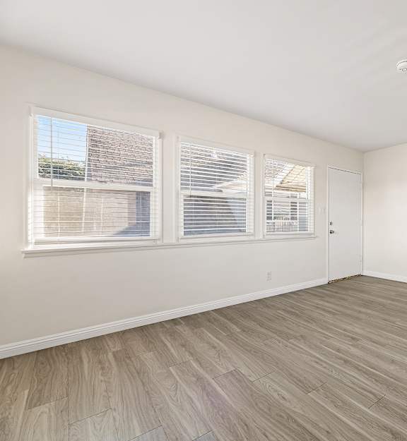 A room with white walls and wooden flooring with a door on the right side.