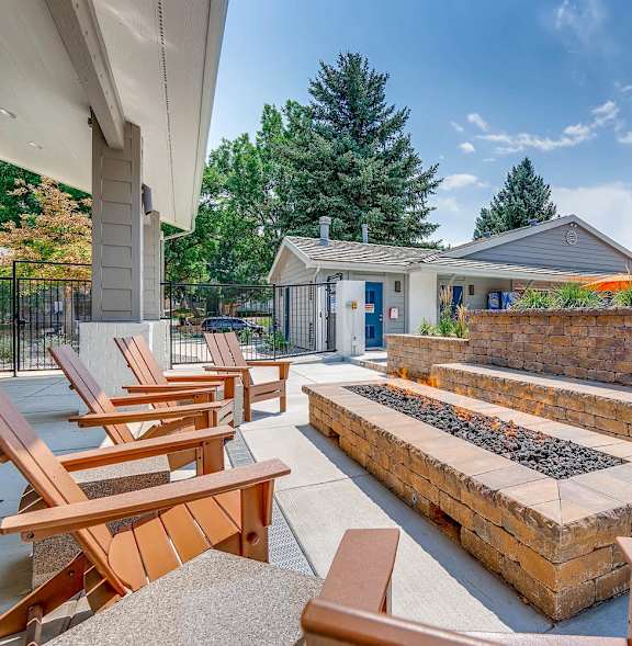 A patio with wooden chairs and a fire pit.