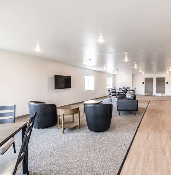 A spacious living room with a long wooden floor and a kitchen area with a black fridge and stove.