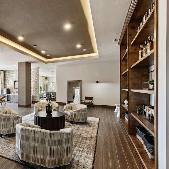 A common room with chairs, bookshelves, coffee tables, and a coffee station at Waterford Market Apartment Homes. 