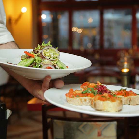 A waiter holding a plate with a salad and a sandwich on it.