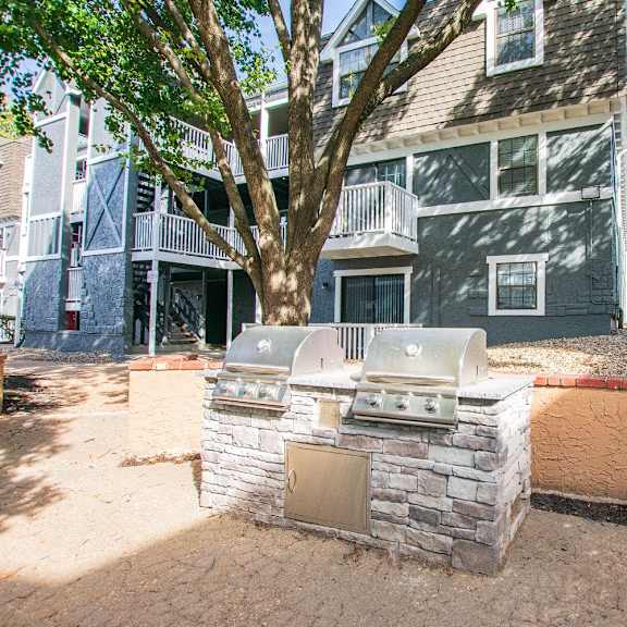 A sandbox with a small building and a tree in front of a grey building.