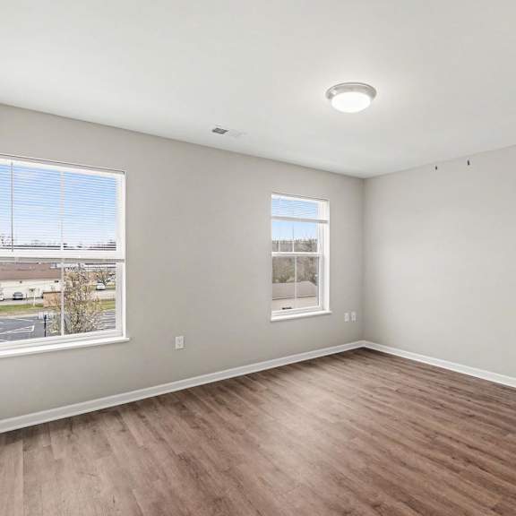 Empty room with wooden flooring and two windows.