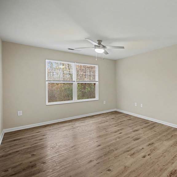 A room with a ceiling fan and a window with a picture hanging on the wall.