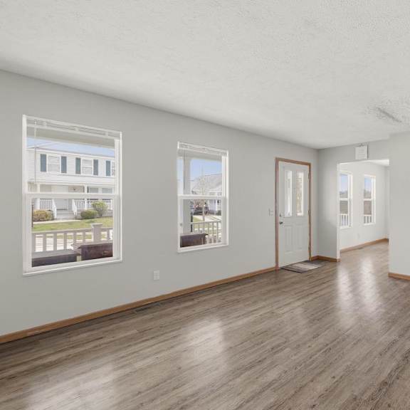 A spacious room with wooden floors and white walls, featuring two windows with pictures on them.