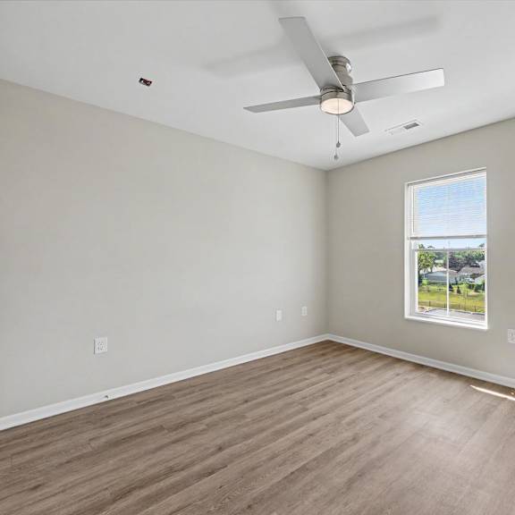 A room with a ceiling fan and a window showing a view of a house.