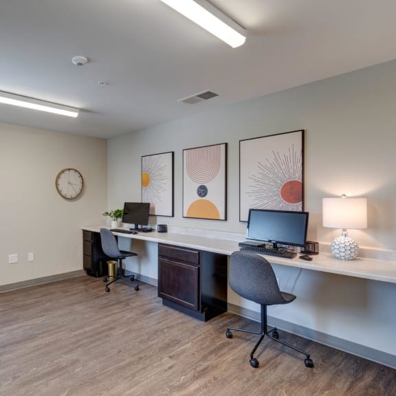 two computers on a long desk with a chair and a clock on the wall