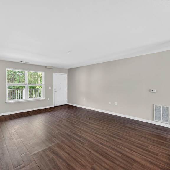 A room with wooden flooring and a window with a view of a fence.