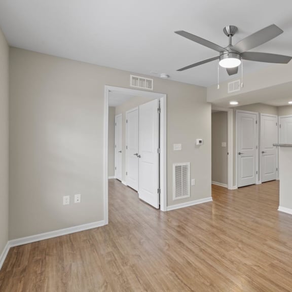 an empty living room with a ceiling fan and a kitchen
