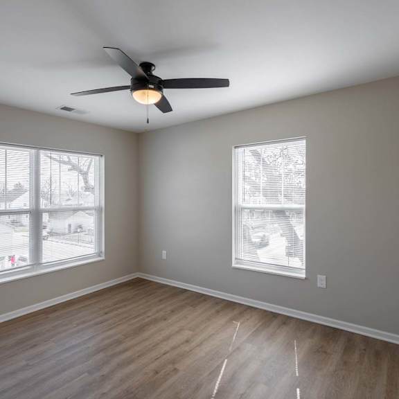 A room with a ceiling fan and two windows.