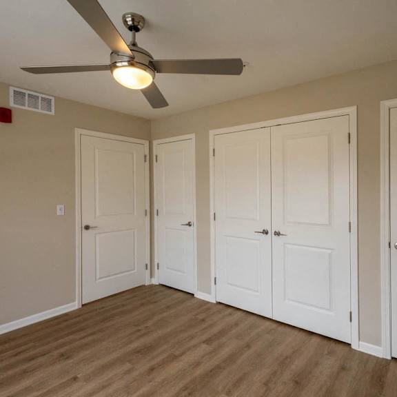 A room with a ceiling fan and four doors.