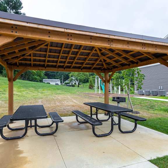 A wooden pergola with a black roof and two picnic tables.