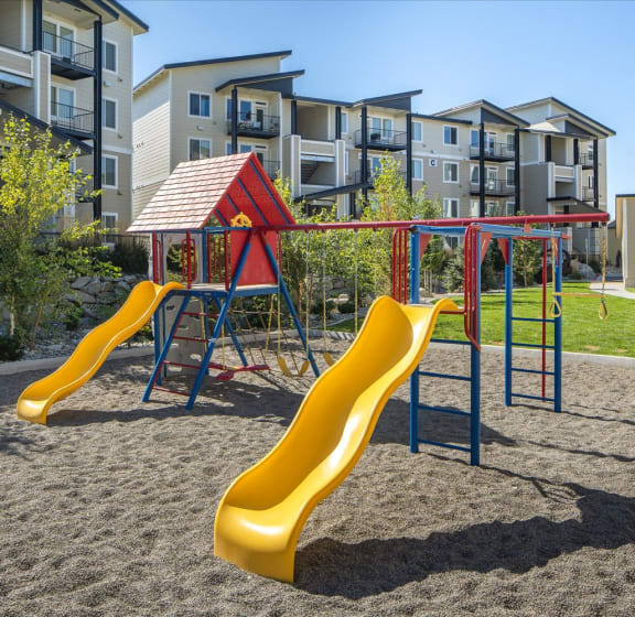 a playground with slides and a swing set in front of an apartment building