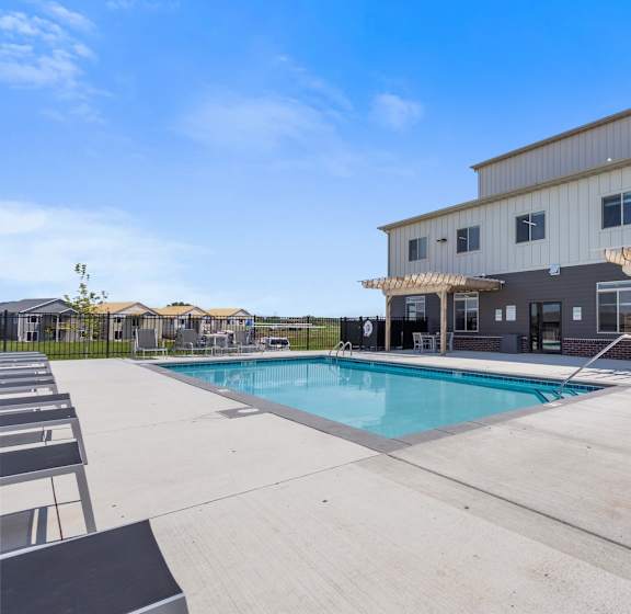 A pool area with sun loungers and a building in the background.