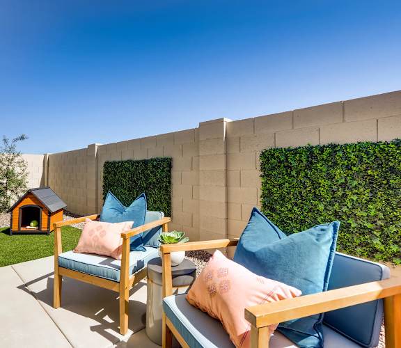 A patio with two chairs and a table with a pink pillow and a blue pillow on it.