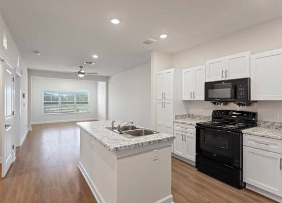 Peaks of Lexington Apartments Kitchen with Black Appliances, Granite Countertops and White Cabinetry and connected living room