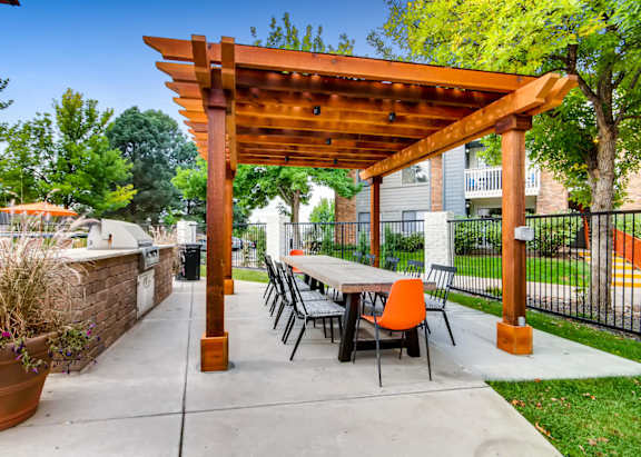 A wooden pergola with a table and chairs is set up in a backyard.