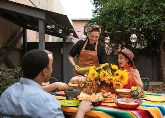 A group of people are gathered around a table with a vibrant tablecloth, enjoying a meal together.