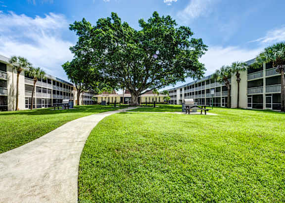 landscaped courtyard with green space and walking paths at Coronado Springs Apartments, a pet-friendly 1- and 2-bedroom community in Palm Springs, Florida.