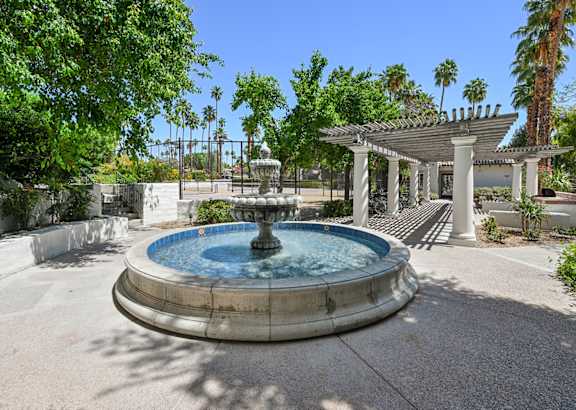 A fountain in the middle of a courtyard with a pavilion in the background.