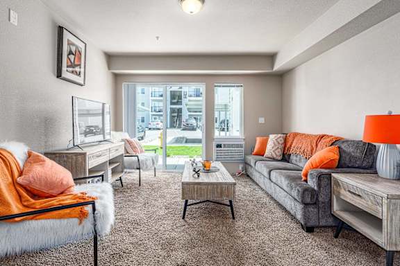 A living room with a grey couch and orange pillows.