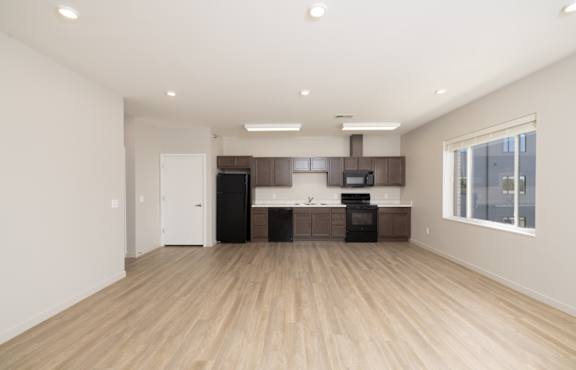 A spacious room with wooden flooring and a kitchen area with appliances.