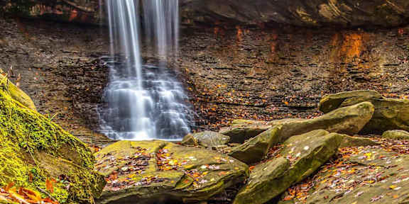 A waterfall flows over a rocky ledge surrounded by autumn leaves.