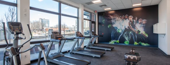 a gym with cardio machines and a wall mural of soccer players